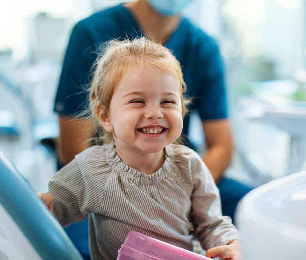 Smiling young girl holding pink folder at dental office with dentist in background.