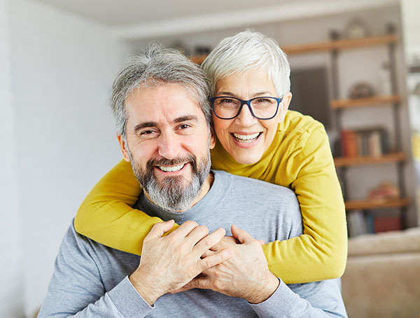 Happy mature couple embracing indoors, smiling at camera in bright home setting.