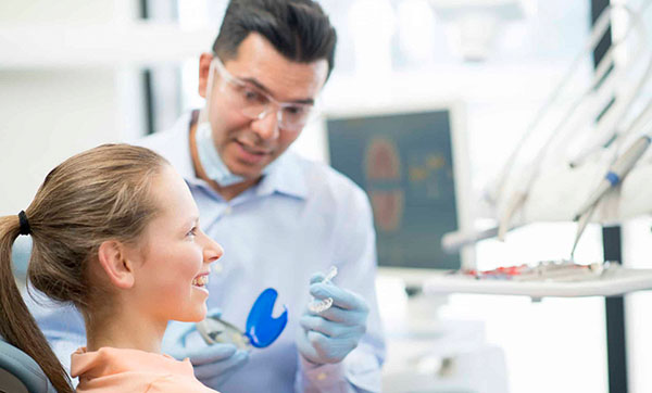 Dentist showing female patient blue dental model in modern clinic treatment room