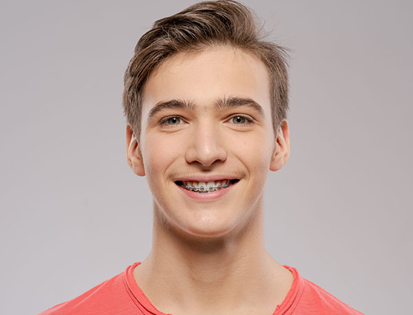 Young man smiling at camera wearing coral shirt against neutral gray background