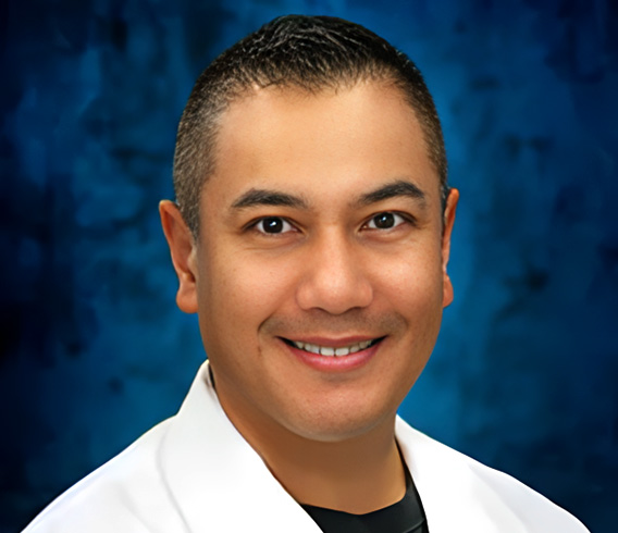 Professional headshot of a man in white coat against blue background for River Rock website.