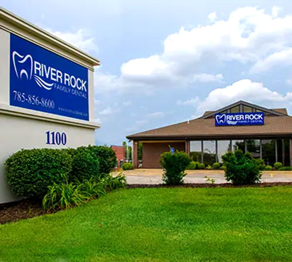 River Rock dental office exterior with blue signage, brick building, and manicured lawn.